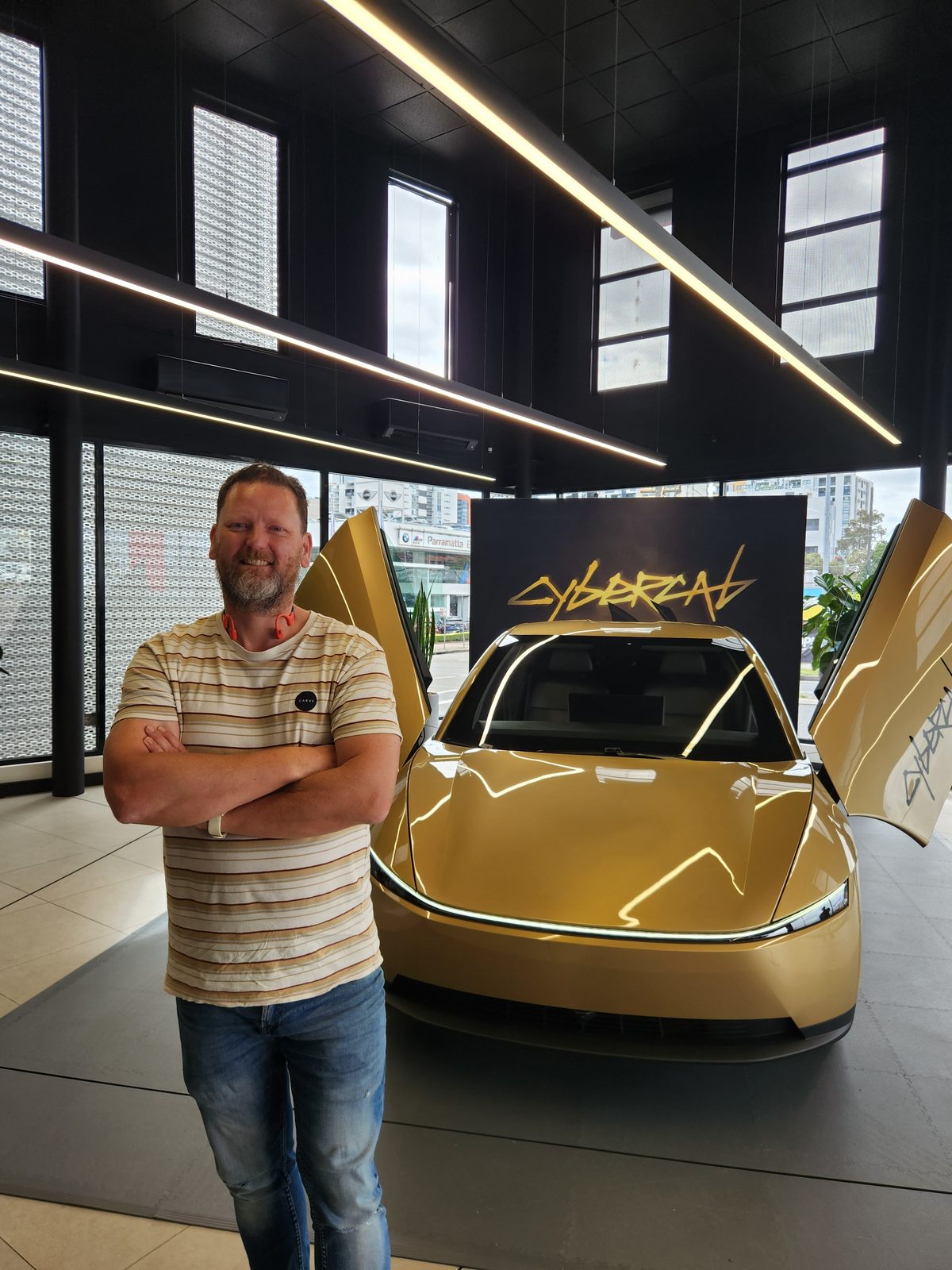 David arms crossed in front of gold Cybercab with butterfly doors open and CYBERCAB backdrop at Tesla Parramatta