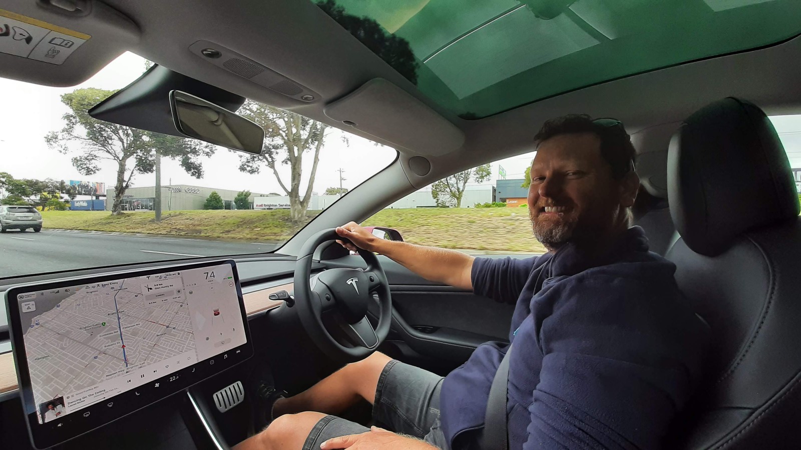 David grinning at the wheel of a hired Tesla Model 3 with the navigation map on the centre screen